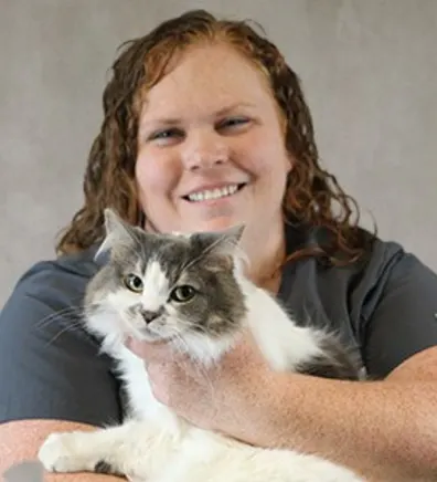 Amy Snyder smiling in front of a grey backdrop holding a white and grey cat